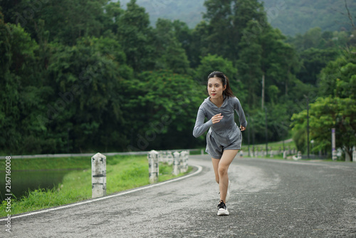 Asian female athlete running on road in green nature park