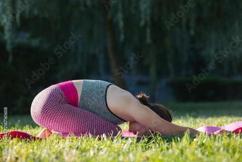 Fotografie Side view of fit woman practicing balasana or child pose on yoga mat upon green