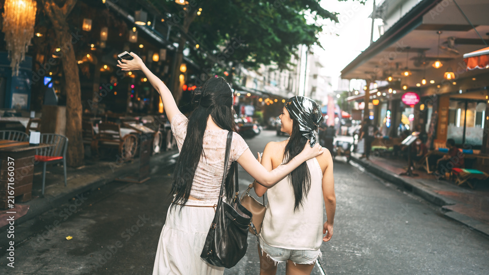 Obraz premium Rear view of two young asian woman hanging out with friends at Khao san walking street hipster style
