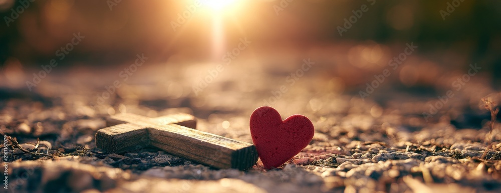 Fototapeta premium Wooden cross and red heart on gravel at sunset 