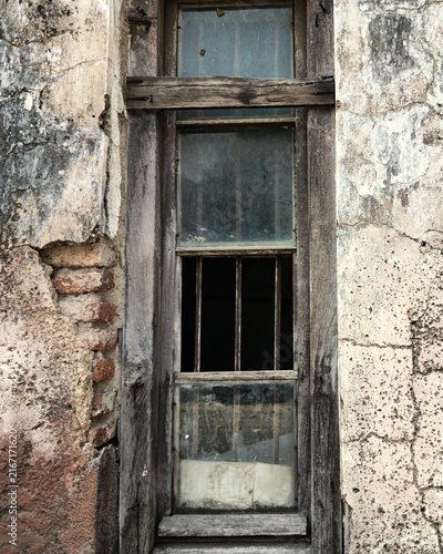 Weathered wooden window set in an aged plaster wall with exposed brick, peeling surfaces, and rustic architectural textures.
