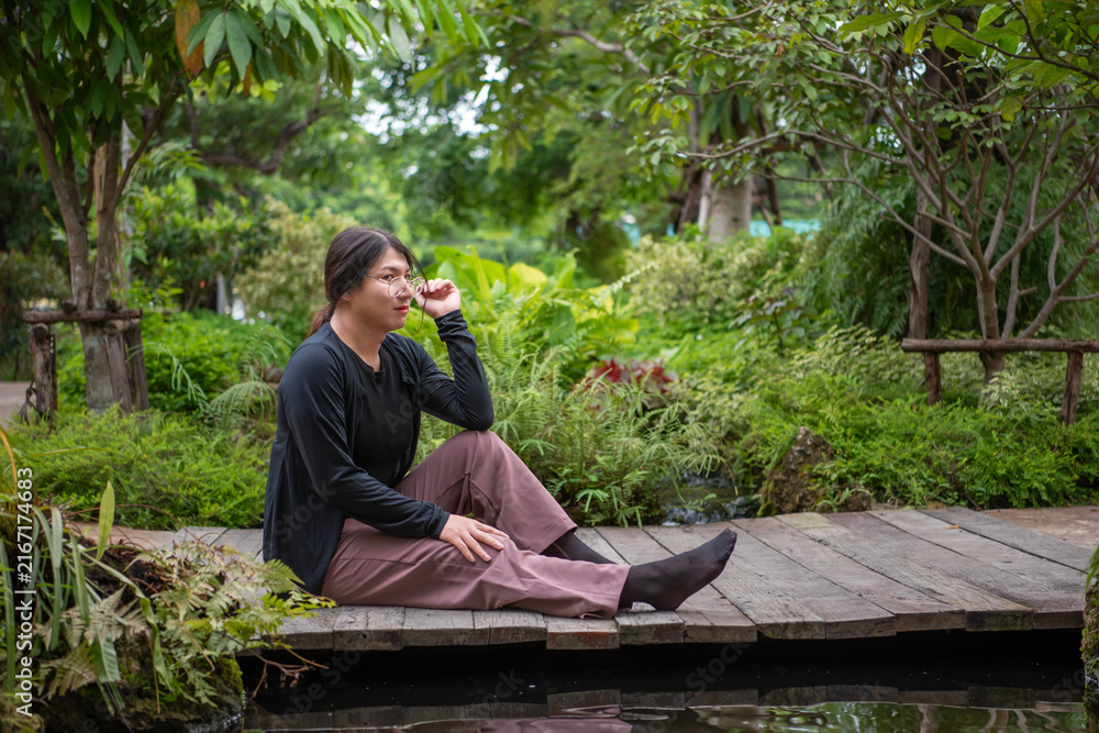 Fototapeta premium LGBTQ person glasses sitting peacefully wooden deck surrounded by lush greenery representing relaxation diversity identity nature wellness outdoor lifestyle
