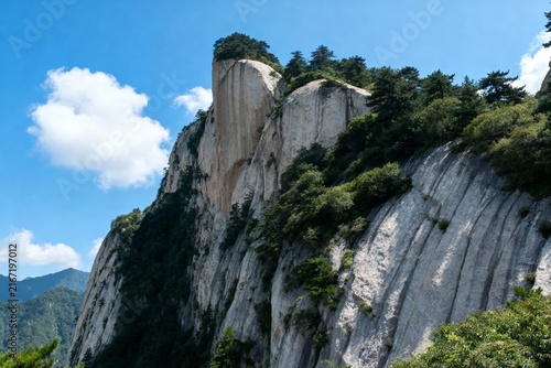 Steep rocky cliff with green vegetation under a clear blue sky