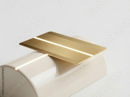 Gold credit card on white cylinder pedestal for luxury banking and premium finance concept