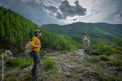 Cuadro en lienzo Two young women with backpacks hiking on top of a rocky cliff overlooking a lush