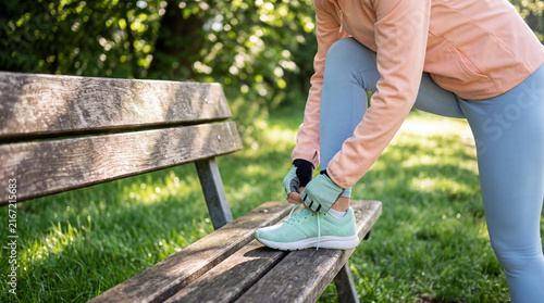 Athletic woman ties a mint running shoe on a wooden park bench in sunshine