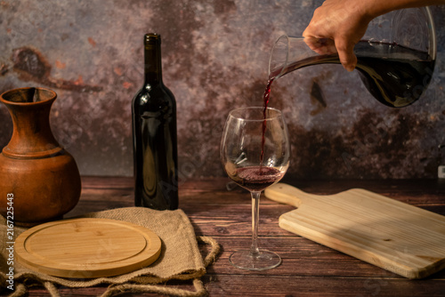 Foto Hand pouring decanted red wine into glass on rustic table