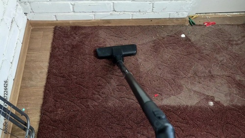 Person vacuuming old and dirty brown rug with a vacuum cleaner, first person view