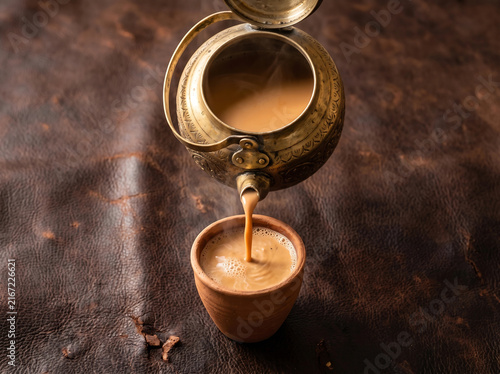 Brass Teapot Pouring Doodh Patti Milk Tea into Clay Cup on Leather Surface