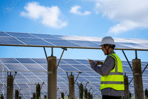 Technician inspecting solar panel farm under clear blue sky