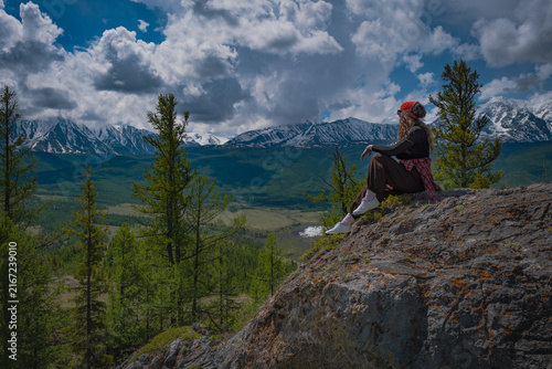 Canvastavla Side view of a young female traveler sitting on top of a rocky cliff and looking