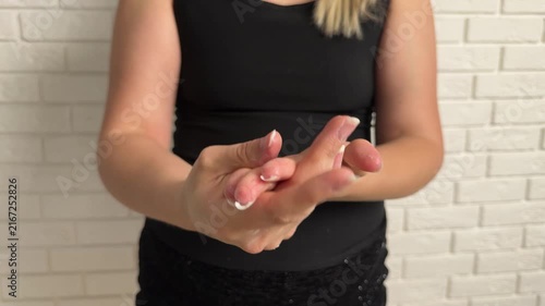 Indoor scene shows woman in sleeveless black top applying lotion or sanitizer across hands and forearms, with visible skin contact, smooth sheen, and simple brick wall backdrop, with woman, lotion