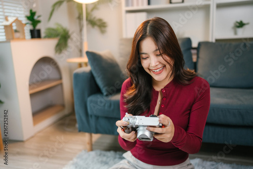 Quadro su tela Asian woman smiling holding camera exploring photography hobby at home