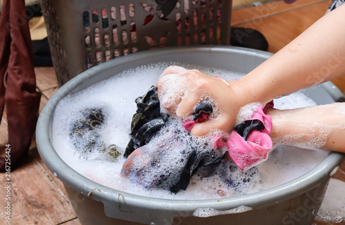 Asian Woman hands washing clothes using detergent in a plastic tub. Female cleaning the dirty clothes in soapy and bubbly soapy water. Household work concept.