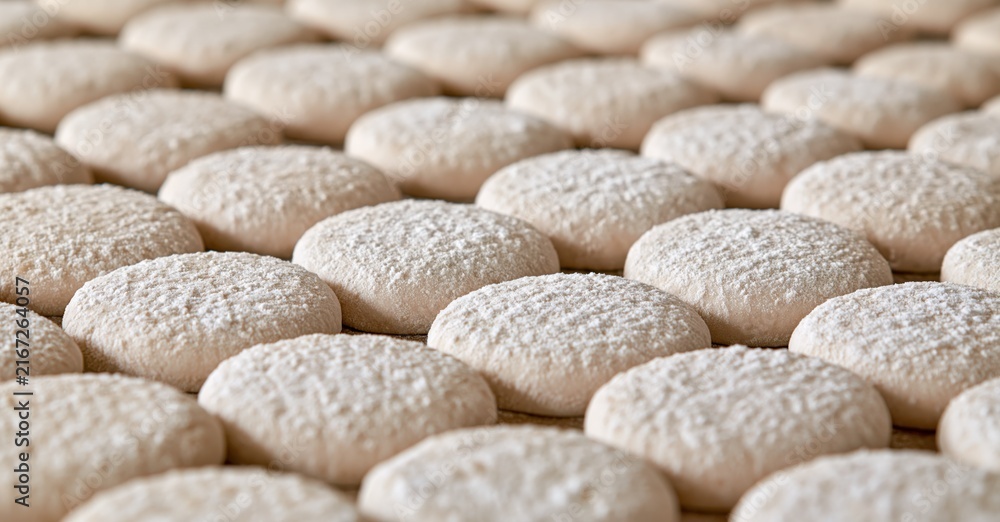 Obraz premium Rows of raw round dough balls dusted with flour