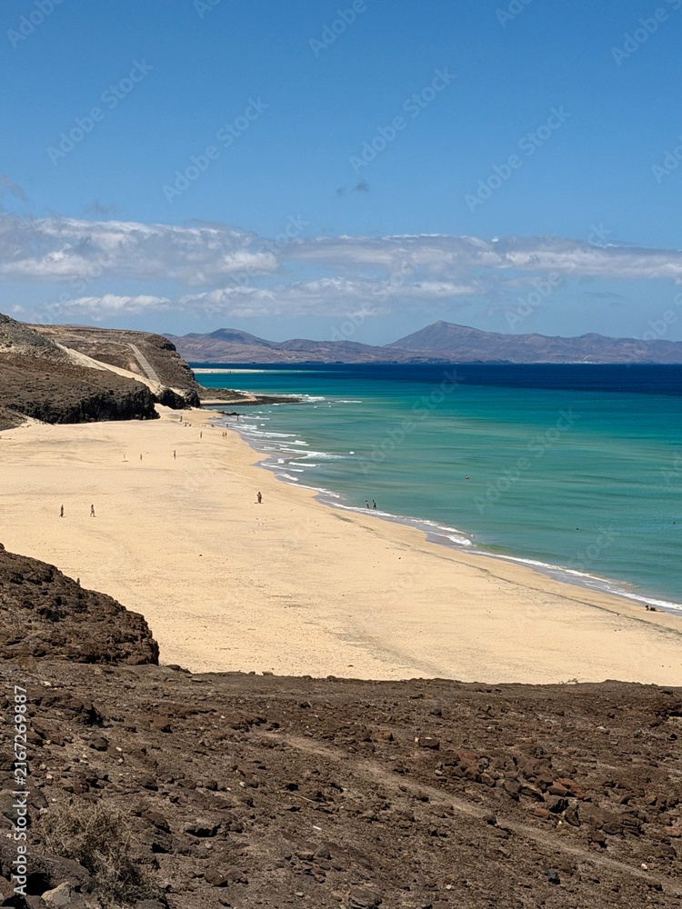 Fototapeta premium Canary Islands. Coastal landscape featuring a sandy beach and turquoise waters, with distant mountains visible under a clear blue sky