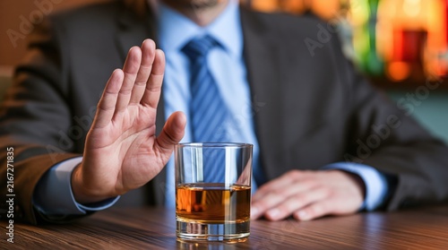 Businessman making stop gesture to glass of whiskey on wooden table