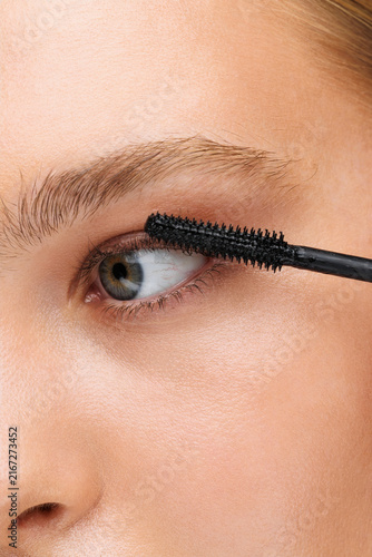 Obraz na plátně Attractive young woman applying mascara against a grey background