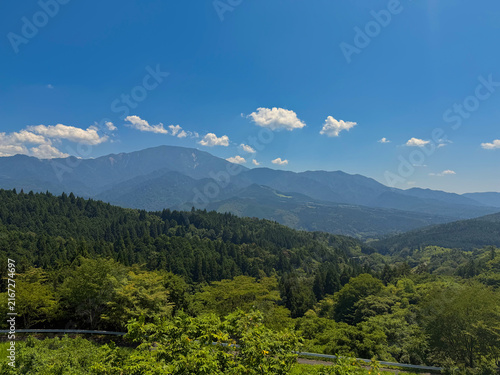 Scenic panoramic view of mountain ranges and lush green forest along Nakasendo trail under blue sky in Japan