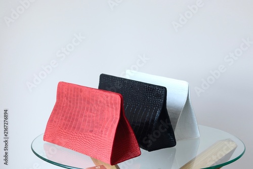 Three elegant crocodile embossed cosmetic clutches in red, black and white displayed on a glass table. Luxury beauty accessories with textured leather design and minimalist premium style.