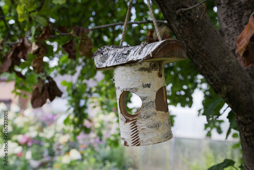 A unique birdhouse made of birch bark hangs from a tree branch.