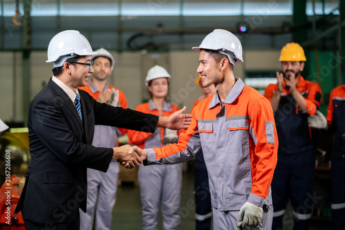 Cuadro en lienzo Factory manager shaking hands with worker while team applauds in celebration, bu