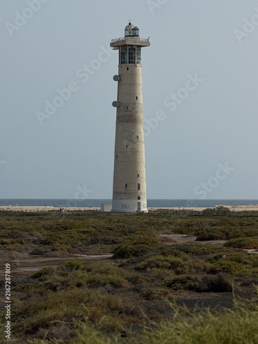 Canary Islands. White lighthouse rises above rocky ground near the coast, surrounded by low vegetation and a clear sky in a coastal environment