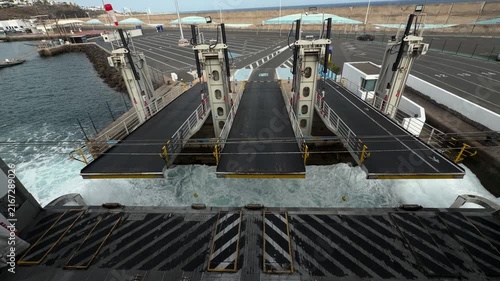 Canary Islands. Ferry terminal features loading ramps extending over water, with workers in safety vests and urban structures visible in the background