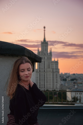 Photography Woman poses on Moscow rooftop with Kotelnicheskaya Embankment Building and warm evening sky behind