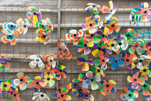 Colorful flower-shaped decorations made from recycled plastic bottles hanging on wire mesh fence.