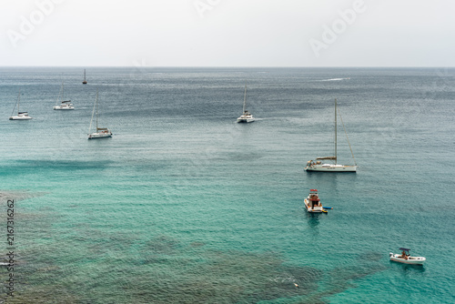 Aerial view of yachts sailboats and motorboats scattered across turquoise sea.