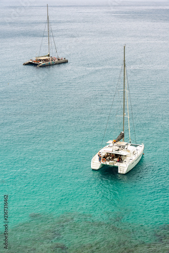Aerial view of two catamarans with tourists anchored in clear turquoise sea.