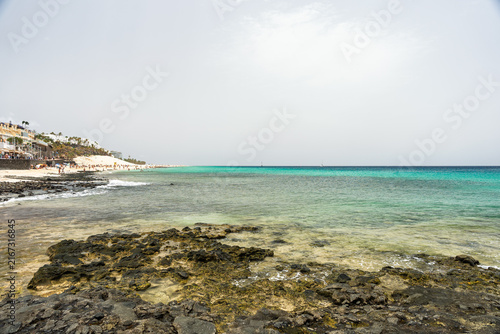 Rocky shoreline overlooking turquoise sea and beachfront resort town in Morro Jable, Fuerteventura.