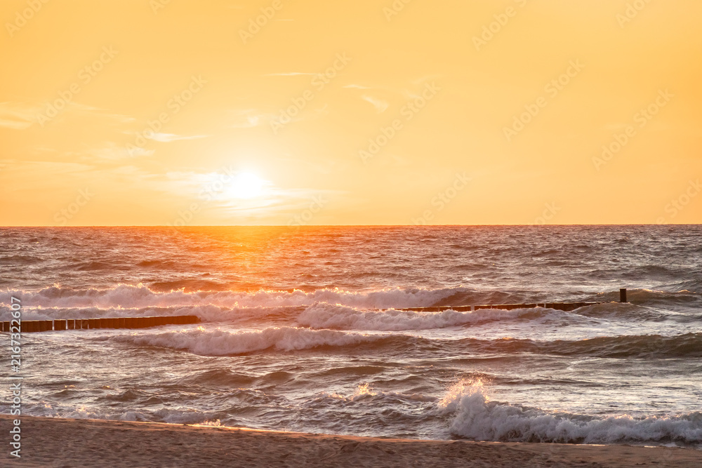 Obraz premium Sunset over the stormy Baltic Sea, high waves over the breakwater, view from the sandy beach.