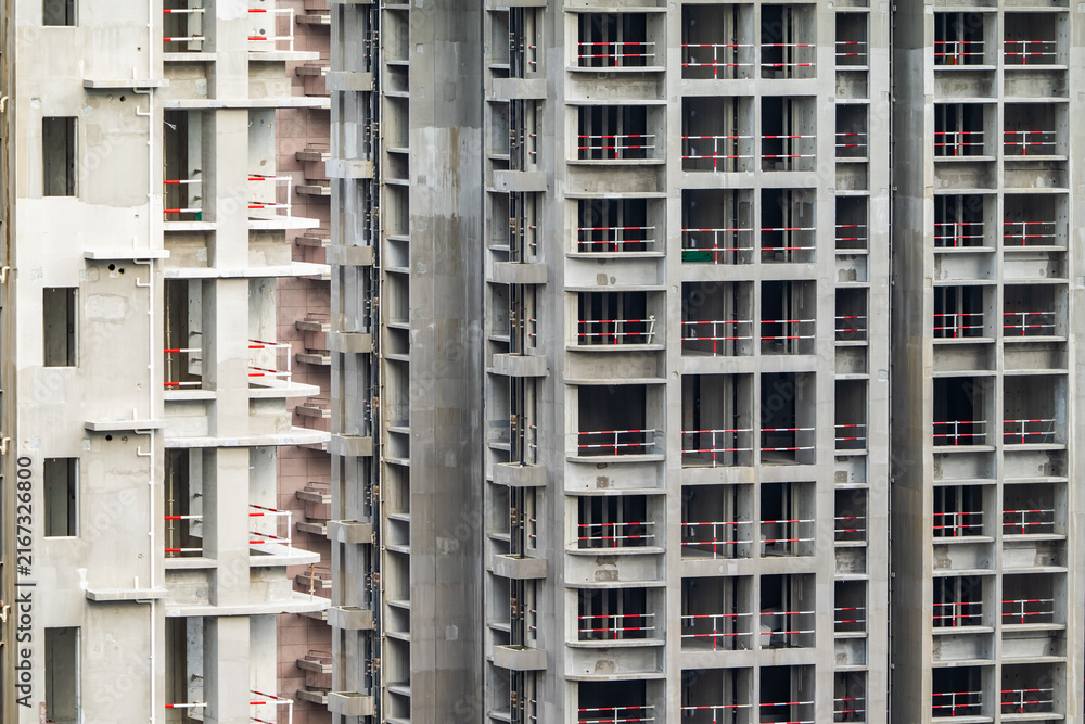 Naklejka premium Apartment or office tall building under construction. Brick walls, glass windows, scaffolding and concrete support pillars