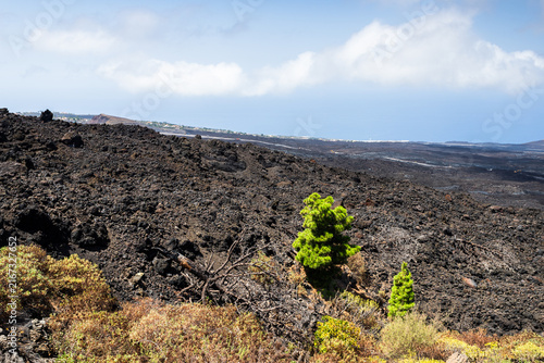 Dark volcanic lava flow fields under cloudy blue sky in La Palma