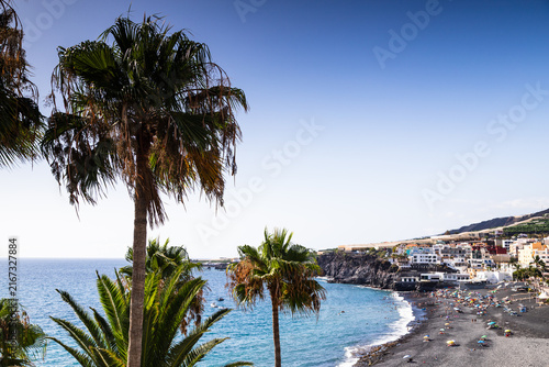 Palm trees framing black sand beach and ocean in Puerto Naos La Palma