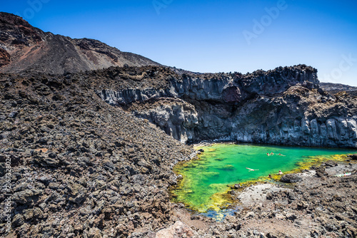 Swimmers enjoying green geothermal sea pool surrounded by dark volcanic rock in La Palma