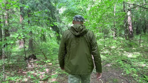 Man striding quickly through the forest from behind. Rear view showing a brisk pace along a wooded path. Active nature walk captured in a green outdoor setting..
