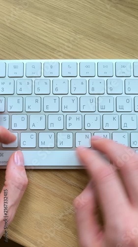 Woman's hands typing on a keyboard in vertical view. Close-up of fingers moving across keys during computer work. Everyday office scene captured from a portrait angle..