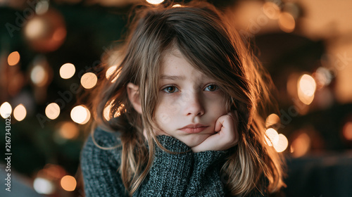 A sad girl in front of a Christmas tree, loneliness, disappointment, depression 
