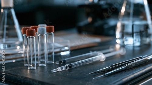 Twilight blue hour still life of toxicology laboratory tools arranged with clinical precision on a dark surface, specimen vials and analytical instruments forming a symbolic