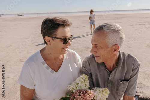 senior couple with bouquet on salt lake, girl runs in background, multigenerational family enjoying sunny outdoor vacation, peaceful retirement, family travel, tourism, senior lifestyle