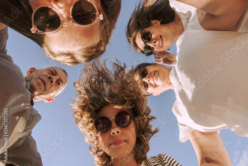 Happy multigenerational family standing in circle and looking down at the camera against a clear blue sky. Grandparents, mother and children in sunglasses together, love, unity, support