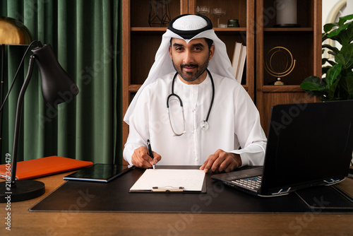 Obraz na płótnie Middle-eastern doctor wearing emirati kandura working in the office - emirati do
