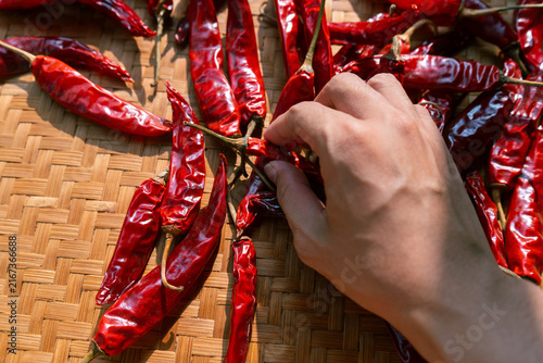 Hand holding dried chili peppers on traditional indonesian woven bamboo basket (besek), prepared to make sambal (spicy sauce), chili oil, or other hot dishes