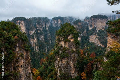 Majestic forest-covered rock formations rise dramatically in a misty mountain landscape