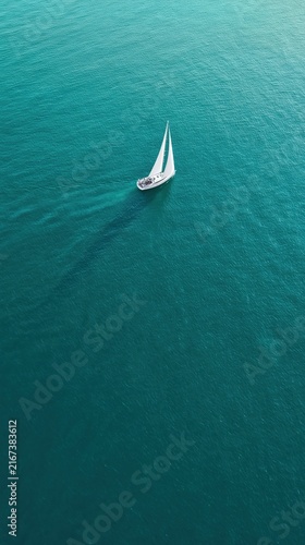 A lone white sailing yacht glides over turquoise sea in a minimalist aerial view. Strong negative space evokes freedom, luxury travel, and serene solitude.