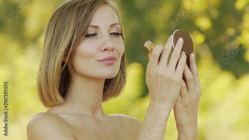 Young beautiful woman puts lipstick on lips