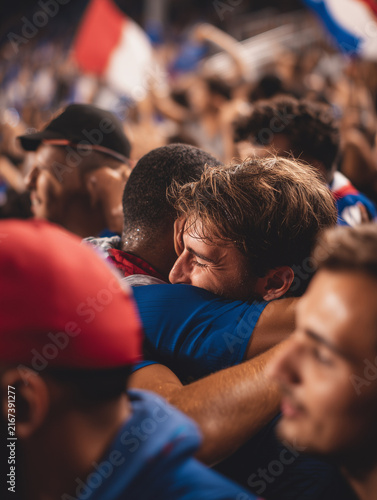 Fans hugging, celebrating victory in a crowded stadium